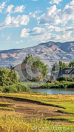 Vertical Homes near a pond and lake against mountain and cloudy blue sky on a sunny day Stock Photo