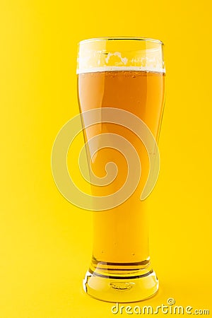 Vertical image of nearly full pint glass of lager beer on yellow background, with copy space Stock Photo