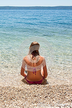 Young female in bikini sitting in shallow sea, vertical Stock Photo