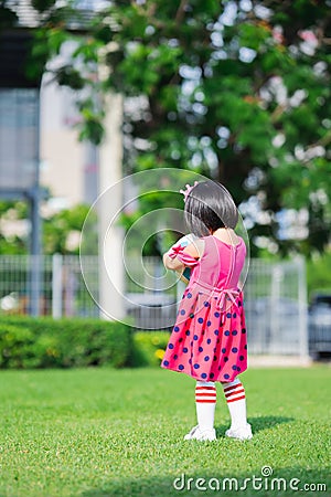 Vertical imaged. Rear back view of Asian girl standing on green laws. Child holding ball in hands. Stock Photo