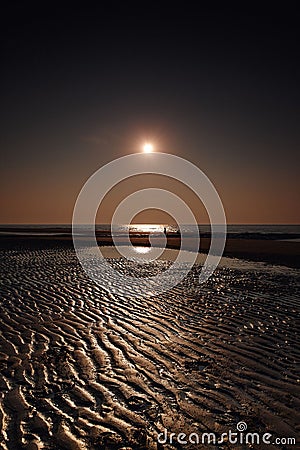 Vertical low-angle of a sunlit seascape with a wet sand dark sky background Stock Photo