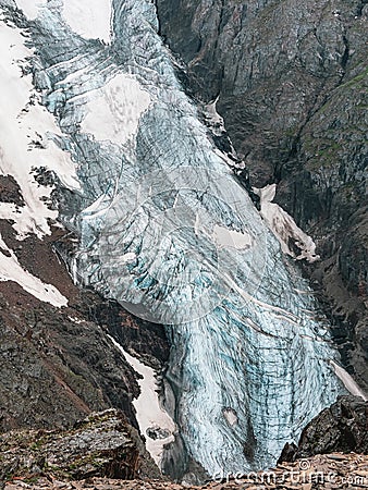 Vertical mountain landscape with blue long vertical glacier tongue with cracks among rocks. Aerial view to large glacier with Stock Photo