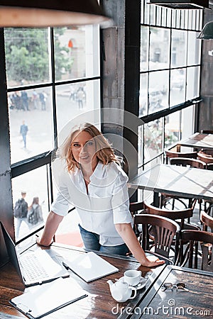 Vertical photo. Businesswoman with curly blonde hair indoors in cafe at daytime Stock Photo