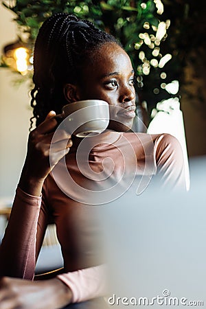 Vertical photo calm, dreaming african afro american young woman with dreadlocks, drinking coffee in cafe. Coffee break Stock Photo