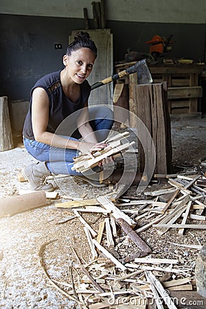 Vertical photograph of a smiling woman crouching on the ground gathering freshly cut firewood to make a fire. equality at work. Stock Photo