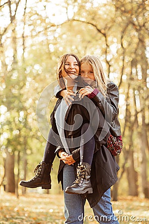 Vertical playful positive, loving, merry family young mother holding daughter on back, promenade in golden autumn forest Stock Photo