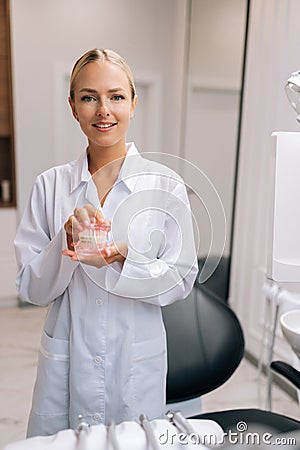 Vertical portrait of attractive female orthodontist doctor in white coat holding human jaws layout model with metal Stock Photo