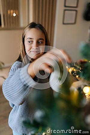 Vertical portrait of cute adorable little girl enjoying process of decorating Christmas tree at home. Cute smiling child Stock Photo