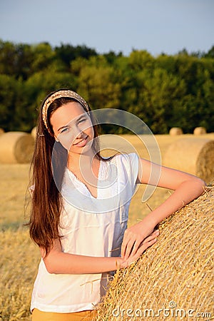Vertical portrait of a girl in a white blouse, standing against a background of bales of straw and smiling, close up Stock Photo