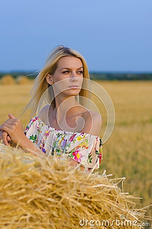 Vertical portrait of a pretty blonde near a haystack against a nature background Stock Photo