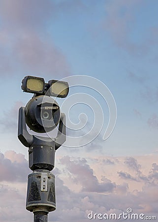 Vertical Puffy clouds at sunset Moving security camera on a post with lights on top Stock Photo