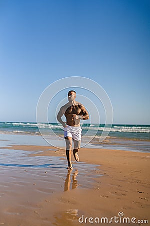 Vertical shot of an attractive topless man with tattoos running on a beach next to a sea Stock Photo