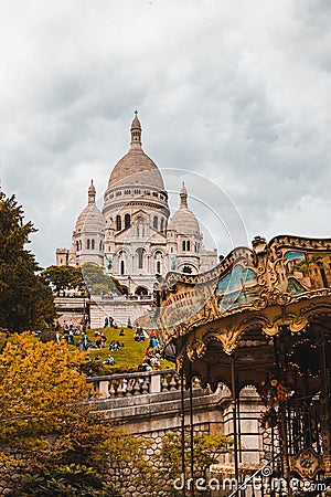 Vertical shot of The Basilica of the Sacred Heart of Paris or Sacre Coeur near a carousel in France Editorial Stock Photo