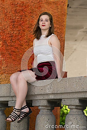 Beautiful young woman in cropped white top and short red skirt sitting on stone balustrade Stock Photo