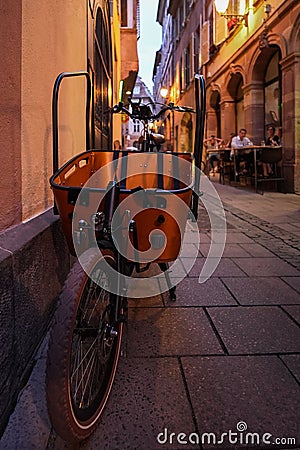 Vertical shot of bicycle with a large basket parked on the street with cafes in Strasbourg, France. Editorial Stock Photo