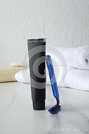 Vertical shot of black tube of shaving cream, razor on the white table and towels, shower sponges on the background Stock Photo