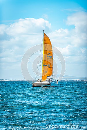 Vertical shot of a boat with an orange sail cruising under a cloudy blue sky Editorial Stock Photo