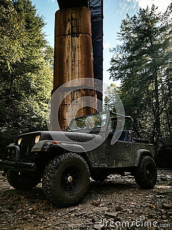 Vertical shot of dark green Jeep Wrangler by wooden construction in the woods Editorial Stock Photo