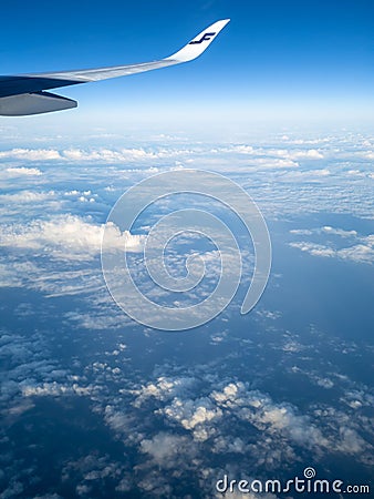 Vertical shot of a Finnair airplane wing flying in the blue sky with white clouds below Editorial Stock Photo