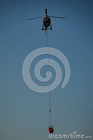 Vertical shot of a fire force helicopter carrying water on blue sky background Stock Photo