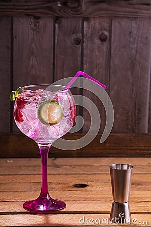 Vertical shot of a glass of pink tonic and gin with raspberries and lime on a wooden table Stock Photo