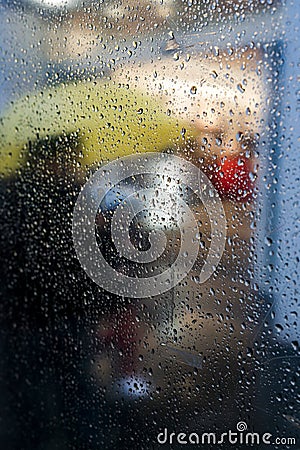 Vertical shot of a glass with raindrops and a person with a yellow umbrella in the background Stock Photo