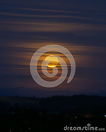 Vertical shot of a glowing yellow moon behind thin clouds in the evening Stock Photo