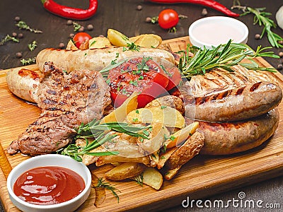 Grilled meat platter with pork and chicken steak, sausages and peasant potatoes with two sauces Stock Photo