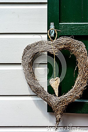 Vertical shot of heart-shaped wreath of branches hanging on a green window against a white wall Stock Photo