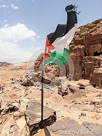 Vertical shot of the Jordanian flag flapping in the wind set atop a rock wall Stock Photo