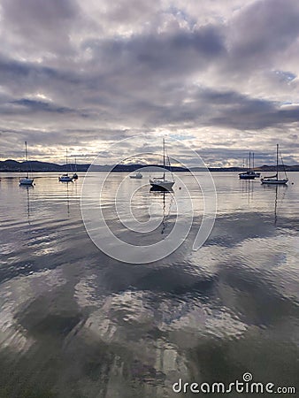 Vertical shot of a lake with silhouettes of boats under a cloudy sky Stock Photo