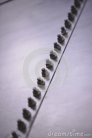 Vertical shot of large screws and nuts in a diagonal line fastened on a steel surface Stock Photo