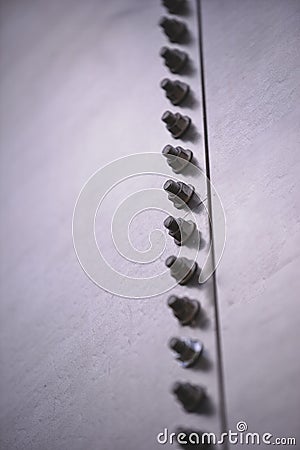 Vertical shot of large screws and nuts fastened on a steel surface Stock Photo