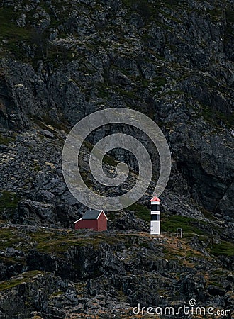 Vertical shot of the Lyngstuva lighthouse and a red small house situated on a rocky mountain, Norway Stock Photo