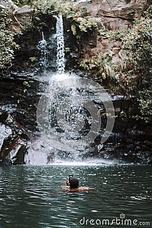 Vertical shot of a male taking a picture of a beautiful waterfall while swimming Editorial Stock Photo