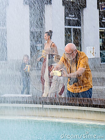 Vertical shot of a man taking a photo of a fountain with a smartphone in Lazarski square, Poznan Editorial Stock Photo