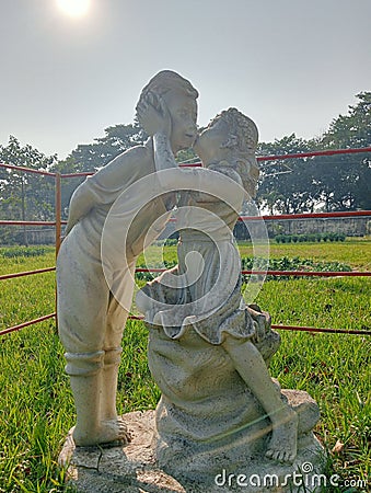 Vertical shot of a marble sculpture of a little girl kissing a boy in the garden. Editorial Stock Photo