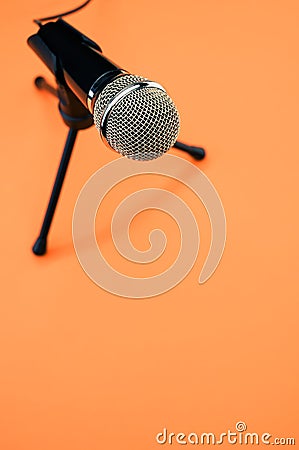 Vertical shot of a microphone on a small stand, on an orange surface Stock Photo