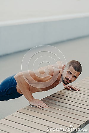 Vertical shot of muscular bearded man stands in plank pose trains chest and arms muscles has hard workout for keeping athletic Stock Photo