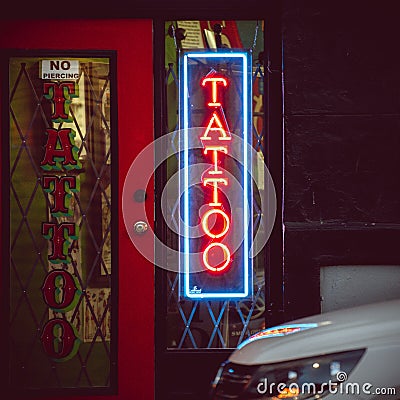 Vertical shot of a neon tattoo salon sign on a door illuminated at night Editorial Stock Photo