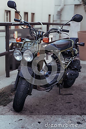 Vertical shot of an old khaki scooter with large headlights parked on the street with chains Stock Photo