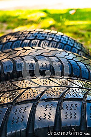 Vertical shot of old used worn car wheel tyres pile stacked in rows on a green background Stock Photo