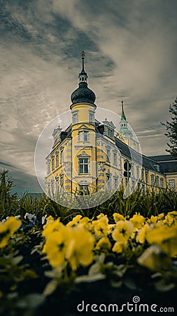 Vertical shot of Oldenburg Palace surrounded by grass and flowers against cloudy sky in Germany Stock Photo