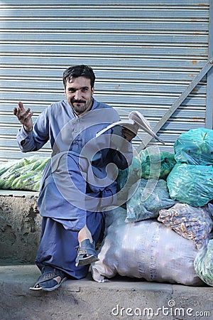 Vertical shot of a Pakistani male with mustache in a market selling fruits and reading book Editorial Stock Photo