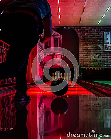 Vertical shot of a person bowling in an arena under bright led lights Stock Photo