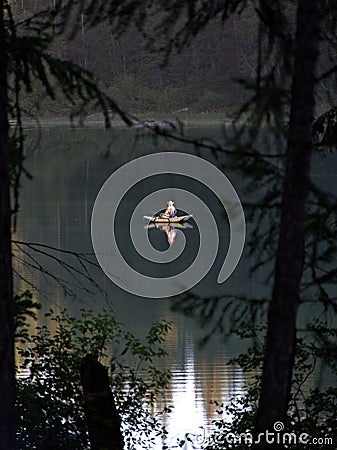 Vertical shot of a person canoeing a tranquil lake surrounded by green trees Stock Photo