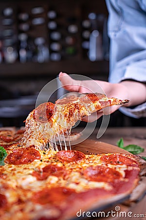 Vertical shot of a person getting a piece of delicious cheesy pepperoni pizza Stock Photo