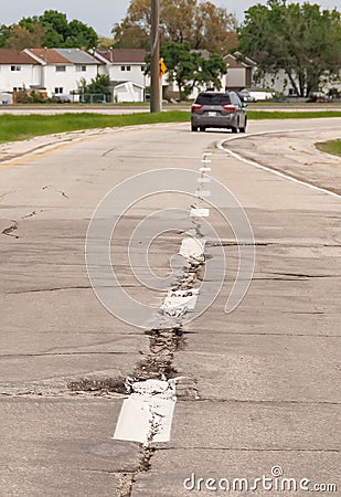 Vertical shot of a road with harmed asphalt coat and a car in the far, Manitoba, Canada Stock Photo