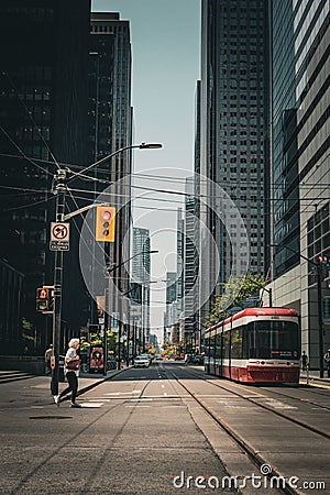Vertical shot of road train tracks in downtown Toronto with a lady passing from traffic lights Editorial Stock Photo