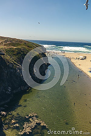 Vertical shot of a rocky cliff and a populated beach in sunny weather Stock Photo